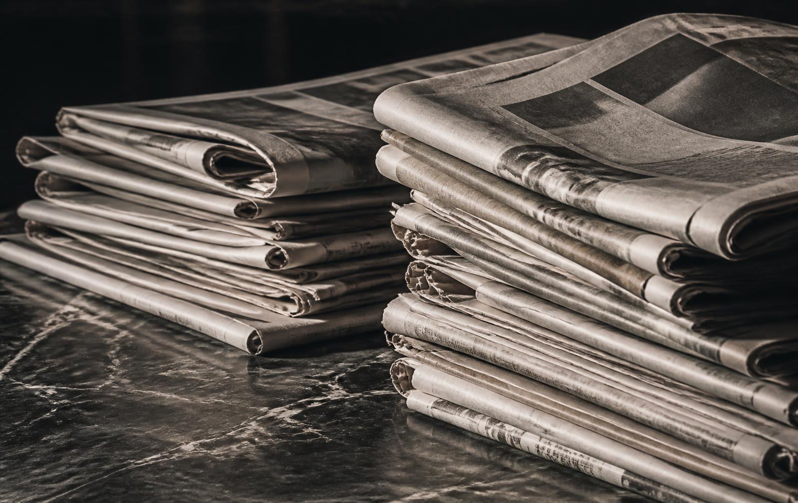 Folded newspapers stacked on a dark marble surface